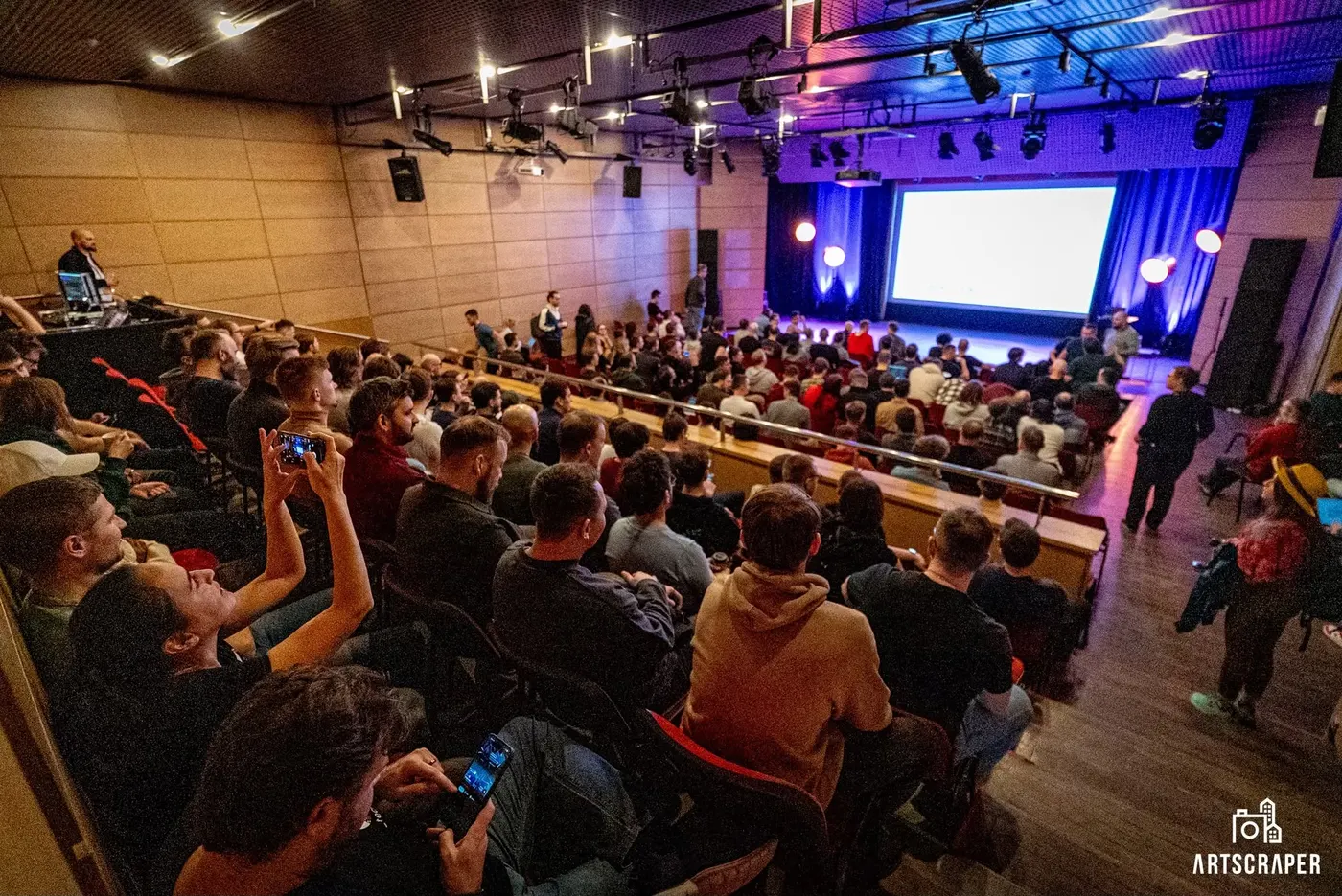 A packed hall seen from the back rows, facing the stage at Winter 2026